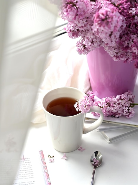 The postcard is beautiful A mug of tea an old book and a bouquet of purple lilac A beautiful still life Spring time The concept of Good morning