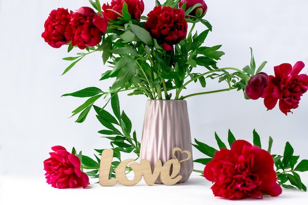 Postcard with a bouquet of scarlet peonies and a wooden inscription love on a white background