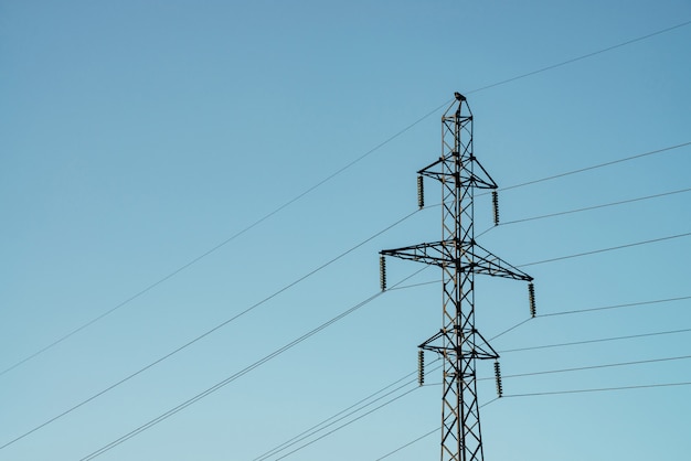 Posts with wires of high voltage on background of blue sky in sunlight. Background image of many wires in sky with copy space. Group of power lines.