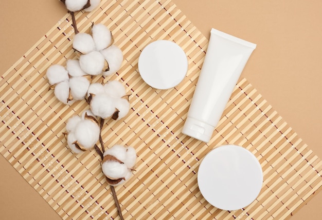Pot en lege witte plastic buizen voor cosmetica op een beige achtergrond Verpakking voor crème gel serum reclame en productpromotie mock-up bovenaanzicht