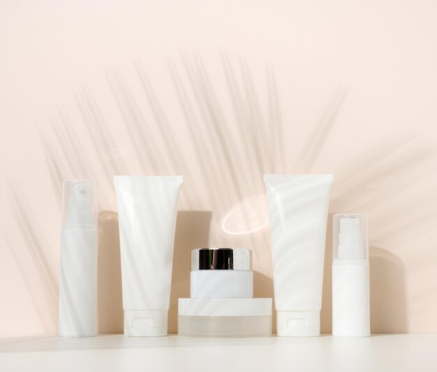 Pot, fles en lege witte plastic buizen voor cosmetica op een beige achtergrond. Verpakking voor crème, gel, serum, reclame en productpromotie, mock-up