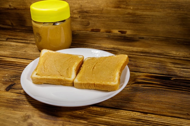 Pot pindakaas en bord met twee sandwiches met pindakaas op houten tafel