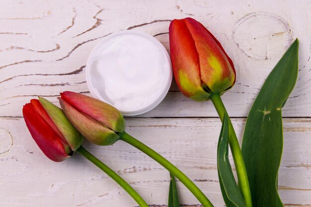 Pot vochtinbrengende crème met rode tulpen op witte houten achtergrond Top view