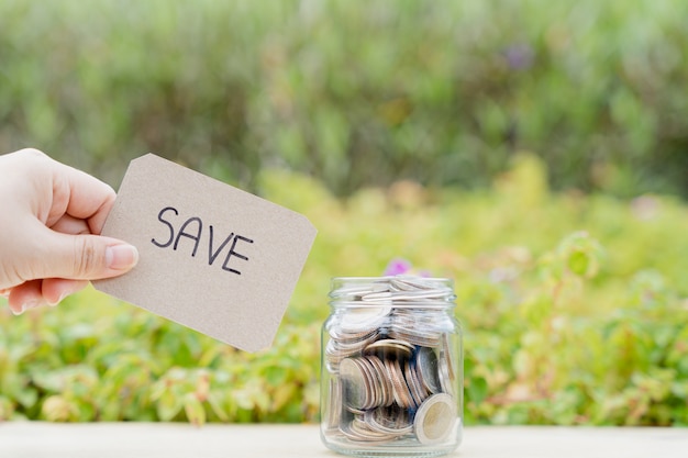 Foto pot vol munten met opslaan woord papier op wazig groene natuurlijke achtergrond. geld besparen en investeringsconcept.