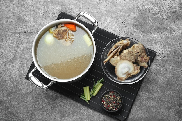 Pot with delicious bone broth and ingredients on grey table flat lay