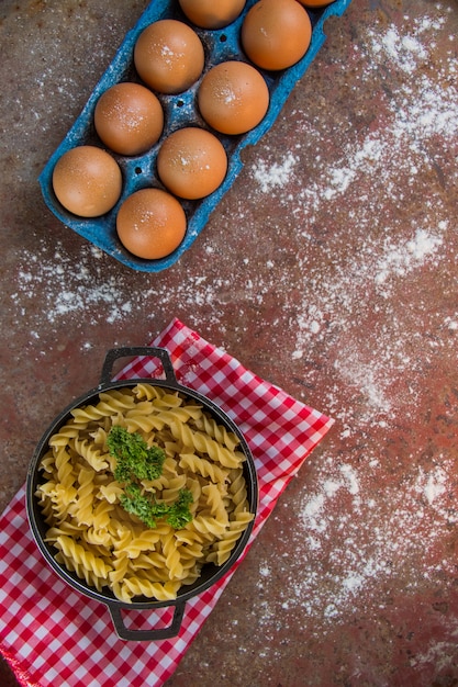 Foto pentola con pasta in viti crude accompagnata da un secchio di uova, farina e prezzemolo