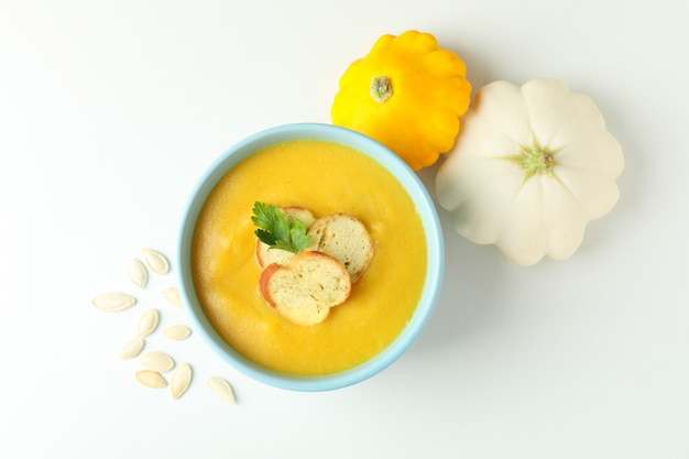 Pot with pumpkin soup and ingredients on white background