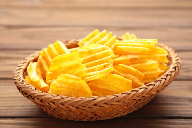 Potato chips in basket on brown wooden wall.