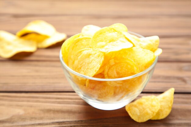 Potato chips on bowl on brown wooden background