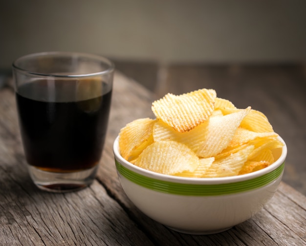 Potato chips in bowl with cola on wooden table .