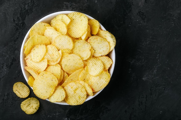 Potato chips Crispy potato chips in bowl on a dark stone concrete background top view with copy space