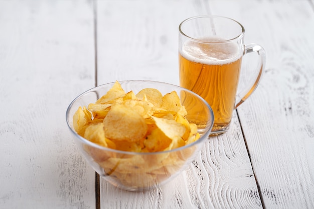 Potato chips en glas bier op een houten tafel.