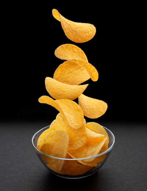 Potato chips falling into glass bowl on black background