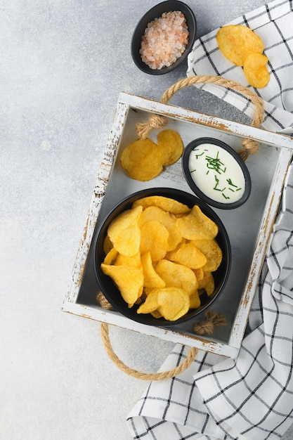 Potato chips Fast food Crispy potato chips ceramic black bowl with sour cream sauce and onions in wooden stand on gray kitchen table concrete background American tradition Hot BBQ Top view