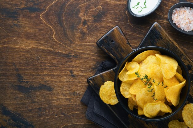 Potato chips Fast food Crispy potato chips ceramic black bowl with sour cream sauce and onions in wooden stand on old kitchen table wooden background American tradition Hot BBQ Top view