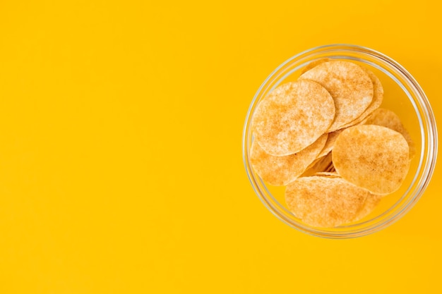 Potato chips in glass bowl on yellow background Fast food