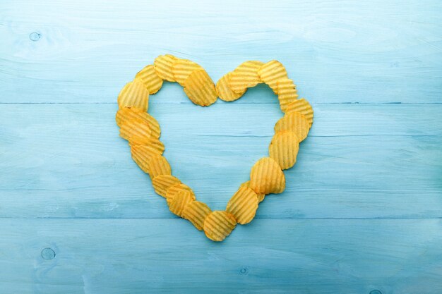 Potato chips heart shape on a blue wooden background. Yellow corrugated salted potato chips as food background.