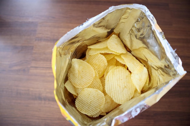 Potato chips in open snack bag close up on table floor