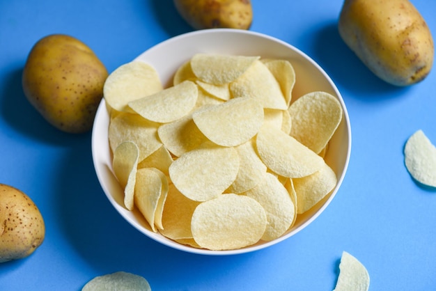 Potato chips snack on bowl Crispy potato chips on the kitchen table and fresh raw potatoes on blue background