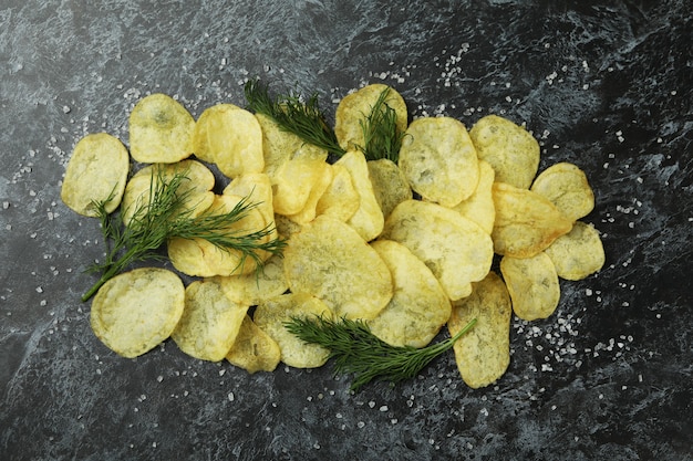 Potato chips with salt and dill on black smokey surface