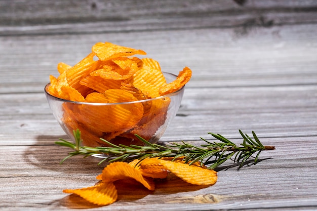 Potato chips with a sprig of rosemary in a glass bowl on a wooden table