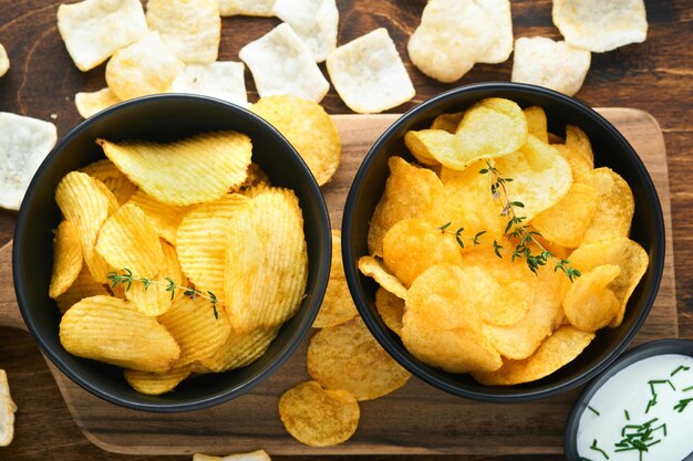 Potato corrugatedchips Fast food Crispy potato chips ceramic black bowl with sour cream sauce and onions in wooden stand on old kitchen table wooden background American tradition Hot BBQ Top view