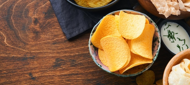 Potato corrugatedchips Fast food Crispy potato chips ceramic black bowl with sour cream sauce and onions in wooden stand on old wooden dark background American tradition Hot BBQ Top view