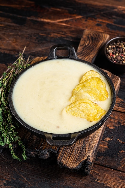 Potato cream soup with potato chips in pan on wooden board. Dark wooden background. Top view.