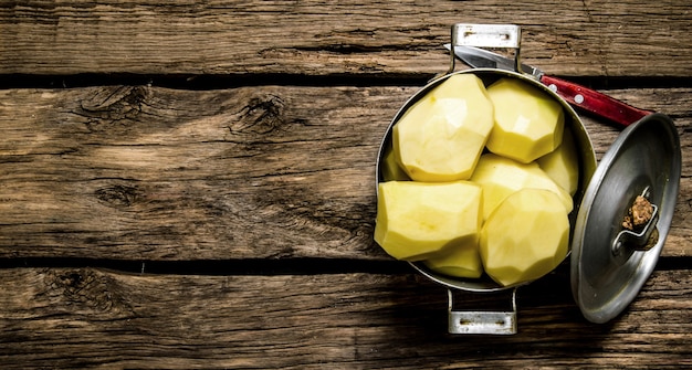 Potato food . Peeled potatoes in an old pan with knife on wooden table . Free space for text. Top view