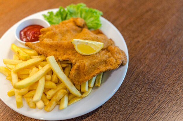 Potato fries with fried meat and red sauce on round white ceramic plate