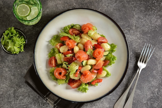 Potato gnocchi salad with tomatoes, cucumber, bell pepper, salmon, and lettuce