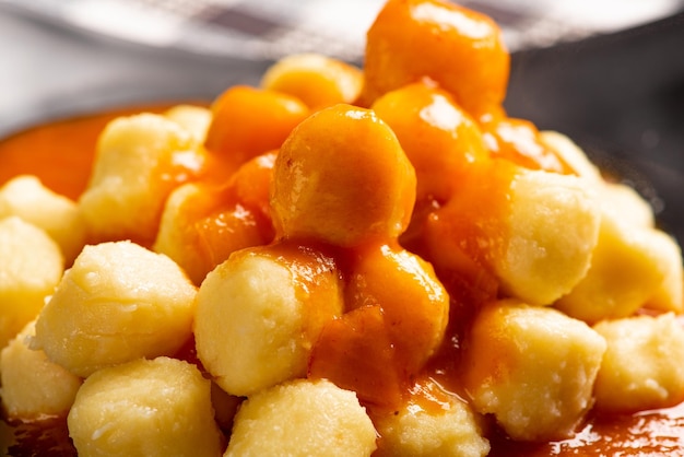 Potato gnocchi with sauce in detail on a black plate over a black and white checkered tablecloth, selective focus.