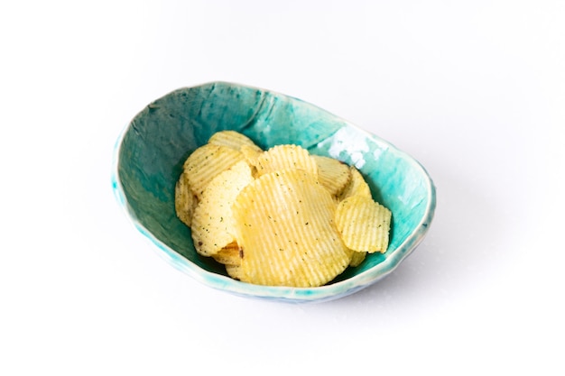 Картофельные рифленые чипсы в самодельной бирюзовой керамической тарелке на белом фоне