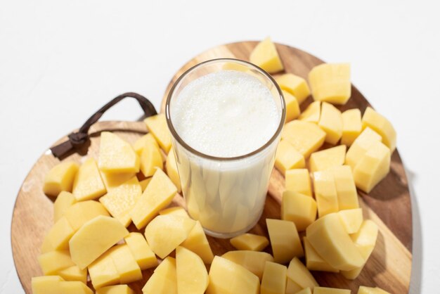 Potato milk concept Alternatieve melk Een glas melk op een houten bord met gehakte rauwe aardappelen