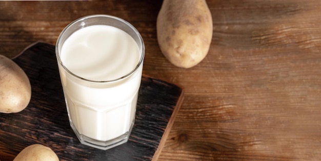 Potato milk glass close up on wooden serving board on wooden background Banner Copy space