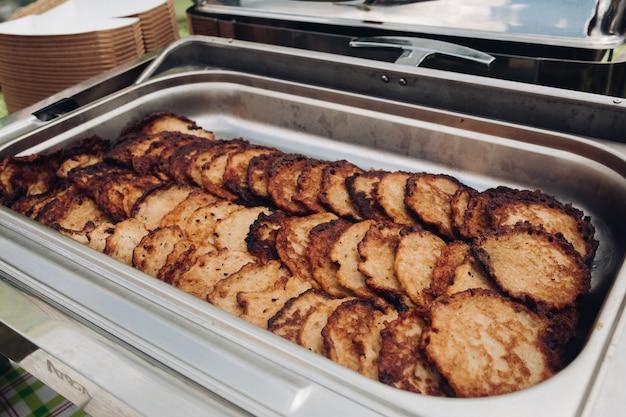 Potato pancakes in metallic container.Close-up of delicious fried potato pancakes in stainless container outdoors. Food festival concept.