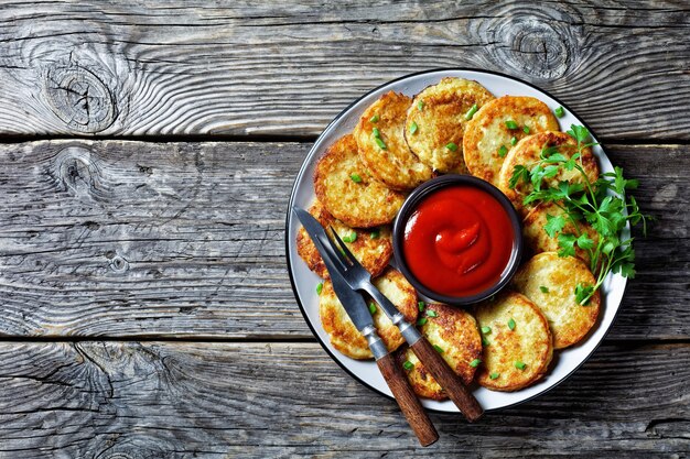 Potato pancakes with cottage cheese with garlic, parsley, served with ketchup on a plate on a wooden background, top view, close-up