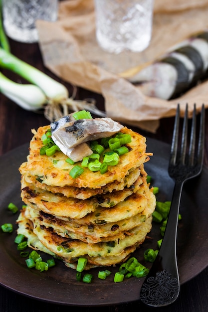 Potato pancakes with herring and onion on a dark background