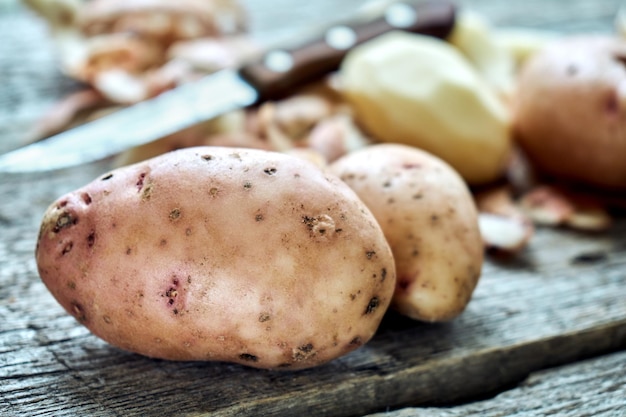 Pelatura di patate sulle tavole di legno grezzo di una tavola di campagna