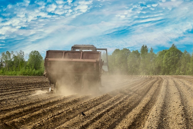 Photo potato planter in agricultural field raises cloud of dust in dry spring during sowing field work