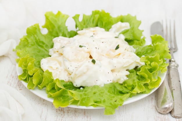 Potato salad on white plate on wooden surface