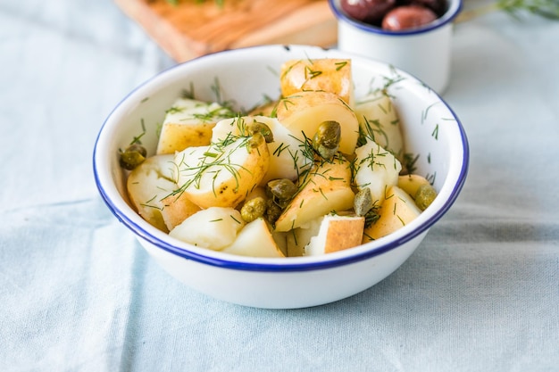 Картофельный салат с укропом и оливками в миске на синем фоне Здоровая пища, веганские и постные рецепты