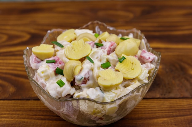 Potato salad with marinated mushrooms, sausage, onion and mayonnaise on wooden table