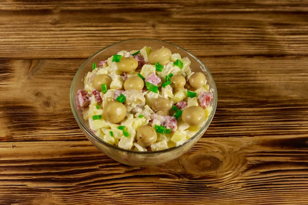 Potato salad with marinated mushrooms, sausage, onion and mayonnaise on wooden table