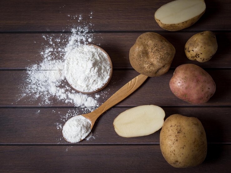 Potato starch with potatoes on a dark wooden background.
