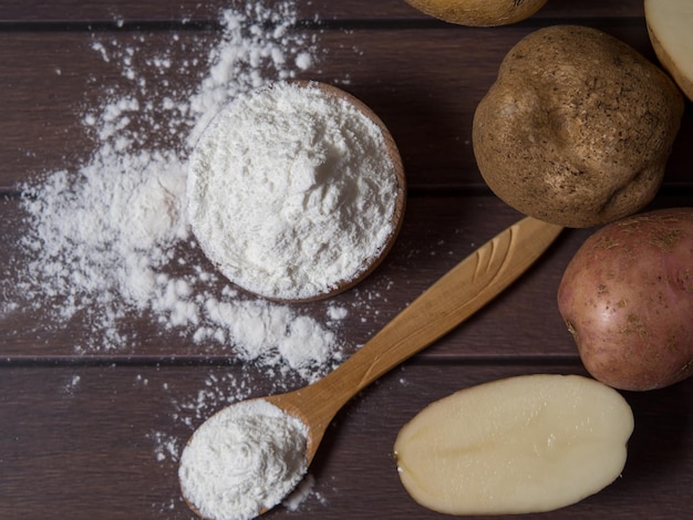 Potato starch with potatoes on a dark wooden background.