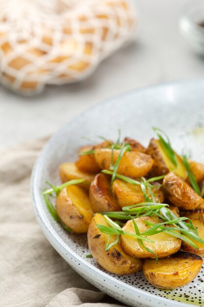 Картофельные дольки, жареные в духовке крупным планом на светлом фоне бетона. Жареный молодой картофель. жарит картошку с зеленым луком.