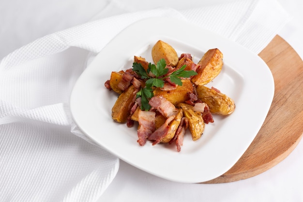 Potato wedges with crispy bacon on white plate