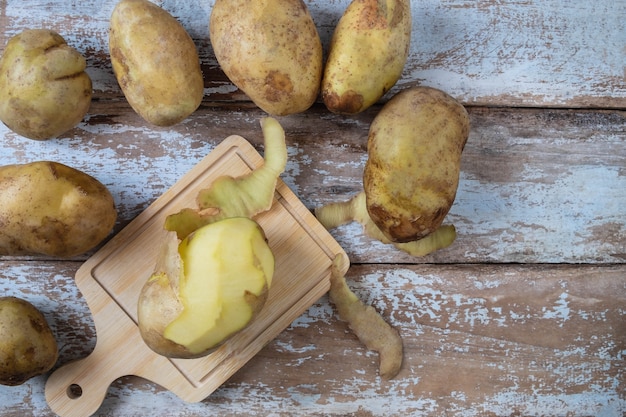 Potatoes are peeled on wooden background.