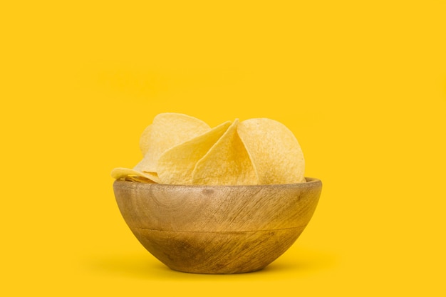 Potatoes chips in a wooden bowl on a yellow background